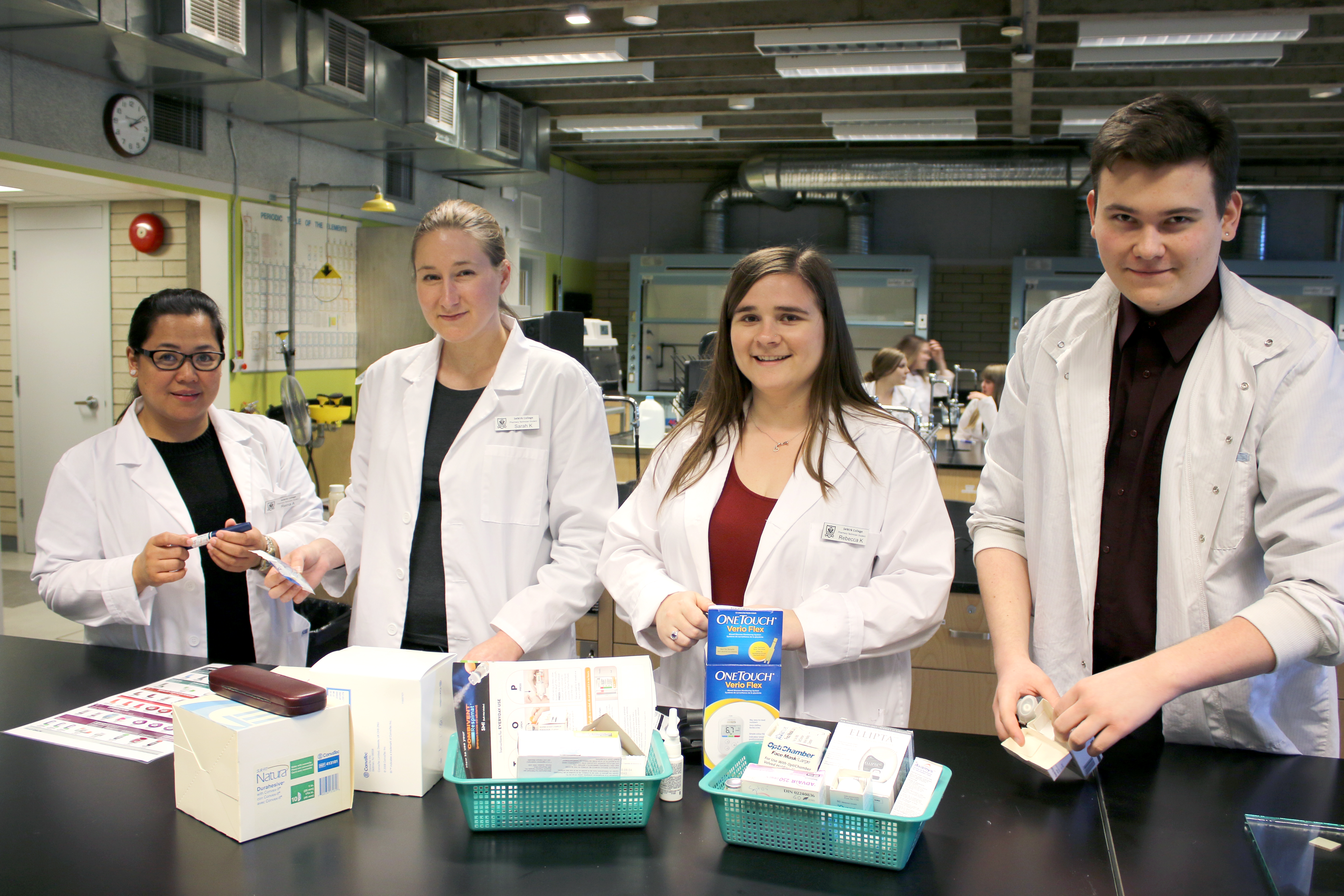 Four pharmacy tech students in a lab wearing lab coats
